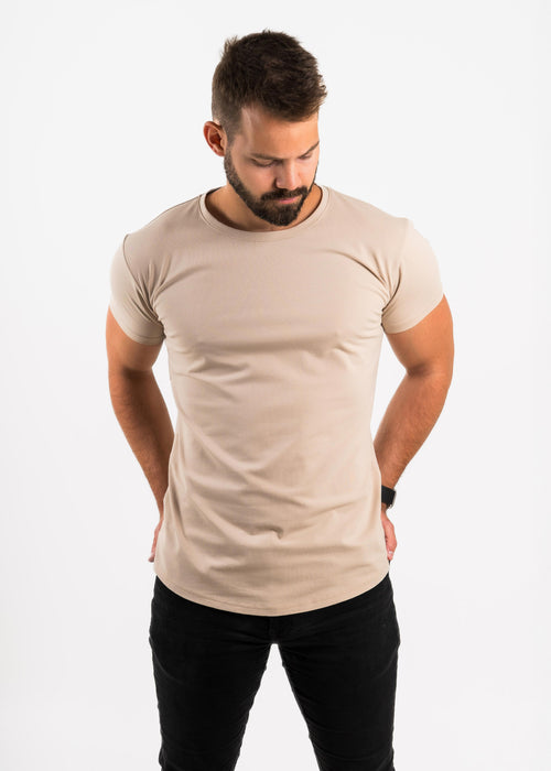 Man wearing a beige Norloom t-shirt and black pants on a white background
